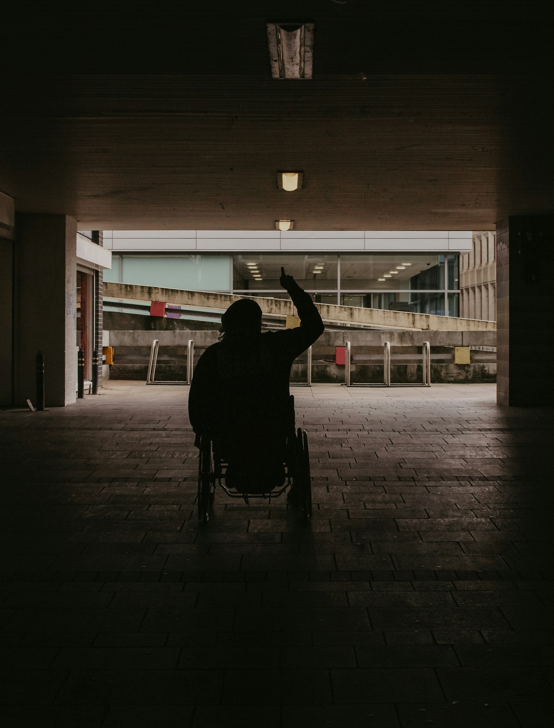 Silhouette of a person in a wheelchair raising one arm high as they roll toward a bright opening